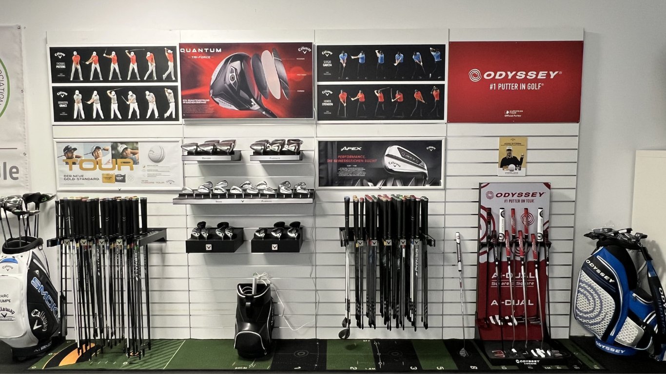 Golf club display wall with organized sets of clubs, bags, instructional posters, and retail signage on white pegboard